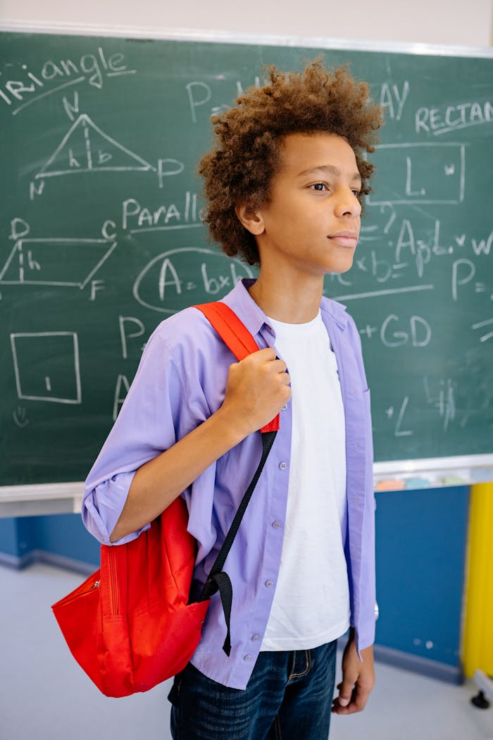 services-04 Teenage student with red backpack standing in front of a blackboard in classroom.